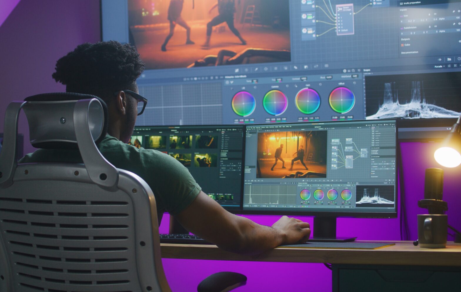 African American editor makes color correction, edits action movie, works at home. Software interface with RGB tools and wheels on computer and big digital screen. Concept of film post production.